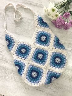 a crocheted purse sitting on top of a wooden table next to some flowers