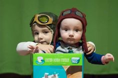 two dolls are posed in front of a green backdrop and one is wearing a pilot's hat