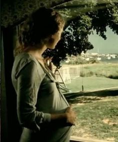 a pregnant woman standing in front of a window looking out at the grass and trees