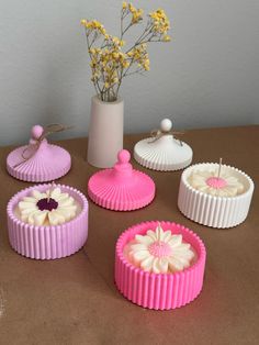 four pink and white cakes sitting on top of a table next to a vase with flowers in it