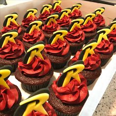 cupcakes with red and yellow frosting are arranged in a box on the table