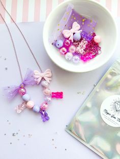 a white bowl filled with beads next to a purple and pink necklace on a table