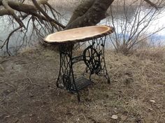 an old sewing machine table sitting on the side of a river bank next to a tree