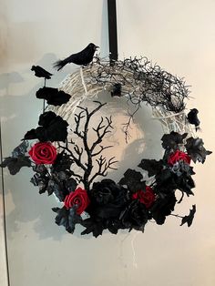 a wreath with red roses and black birds hanging from it's sides on a wall