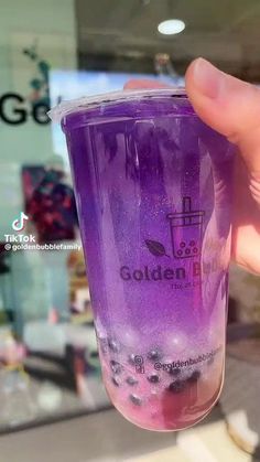 a person holding up a purple cup in front of a store window with the words golden on it