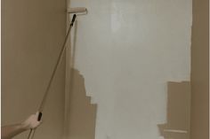 a person using a paint roller to paint a wall in a bathroom with white walls