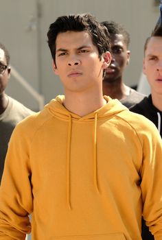 a young man in a yellow hoodie is looking at the camera with other men behind him