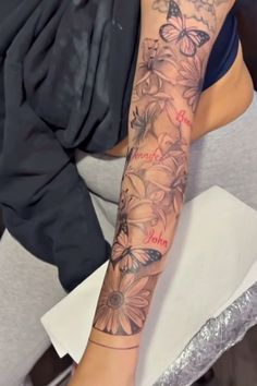 a woman's arm with flowers and butterflies tattooed on her left arm, while sitting in a chair