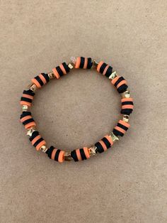 an orange and black beaded bracelet with gold accents sits on a beige carpeted surface