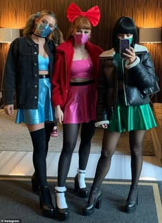 three women in costumes standing next to each other with masks on their faces and looking at a cell phone