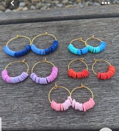 six pairs of hoop earrings in different colors on a wooden bench with gravel behind them