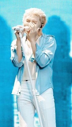 a woman in white pants and a blue jacket holding a microphone with her right hand