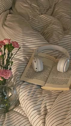 an open book on a bed with flowers in a vase and headphones laying next to it