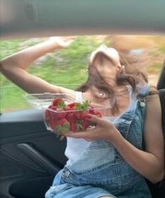 a woman sitting in the back seat of a car holding a bowl of strawberries