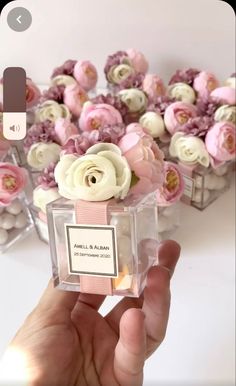 a person is holding a small glass box with flowers in it and there are other boxes behind them