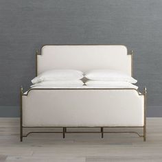 a bed with white linens and pillows on it, against a gray wall in an empty room