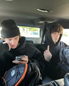 two young men sitting in the back seat of a car, one holding a cell phone