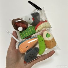 a hand holding several small stuffed animals in a clear bag on a white table top