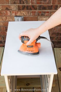 a person using an electric sander on top of a white table next to a brick wall