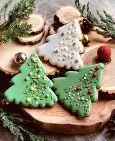 christmas cookies decorated with green and white icing on a wooden platter surrounded by pine branches