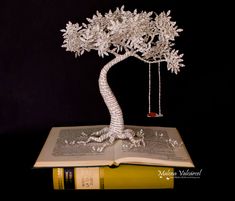 an open book with a tree on top of it and a swing in the middle