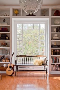 a wooden bench sitting in front of a window next to a book shelf filled with books