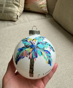 a hand holding a glass ornament with a palm tree painted on it