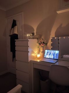 a laptop computer sitting on top of a white desk next to a dresser and mirror