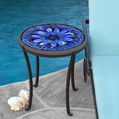 a small table with a blue flower on it next to a swimming pool and lounge chair