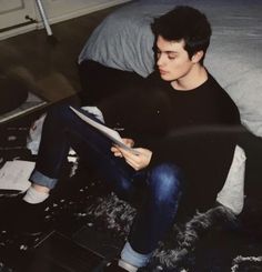 a young man sitting on top of a bed holding a paper in his hand and reading