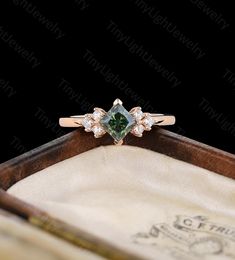 an engagement ring with a green and white diamond in it on top of a wooden box