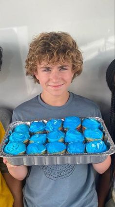 a young boy holding a tray of blue cupcakes