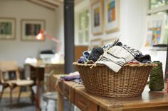 a wicker basket filled with yarn sitting on top of a wooden table next to chairs