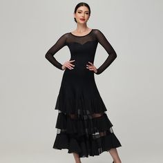 a woman wearing a black dress with sheer sleeves and tiered ruffles on the skirt