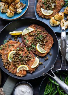 two fish cakes with lemon wedges and green beans on a plate next to other food