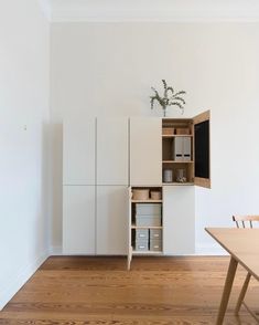 an empty room with white walls and wooden floors is shown in this image, there are two chairs next to the cabinet