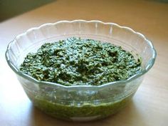 a glass bowl filled with pesto on top of a wooden table