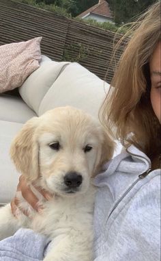 a woman holding a puppy in her arms on a couch with the dog looking at the camera