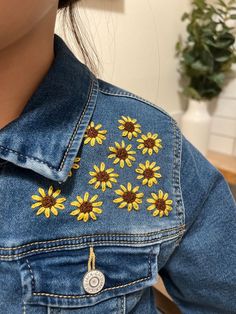 a woman wearing a jean jacket with sunflowers on it's back pocket