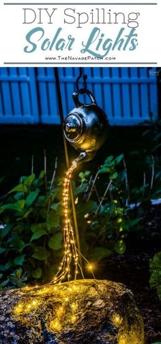 a light up teapot sitting on top of a rock in the middle of a garden