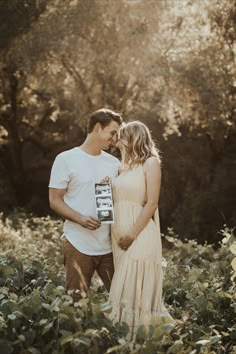 a man and woman standing next to each other in front of trees holding a camera