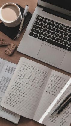 a laptop computer sitting on top of a wooden desk next to papers and coffee cup