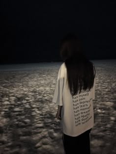 a woman standing in the middle of a field at night with her back to the camera