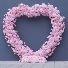 a large heart made out of pink flowers on a gray wall with a wooden floor