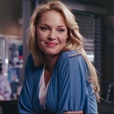 a woman with blonde hair wearing a blue jacket and smiling at the camera in a kitchen