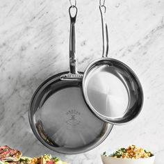 stainless steel pots and pans hanging from hooks on a marble counter top with bowls