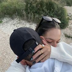 a man and woman hugging each other while wearing sunglasses on top of a hill next to the ocean