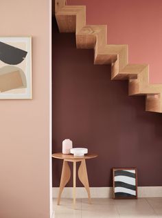 a wooden table sitting under a stair case next to a wall with pink paint on it