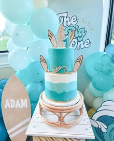 a blue and white cake sitting on top of a wooden table next to some balloons