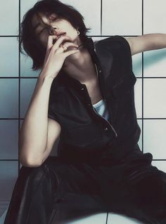 a woman sitting on top of a white tiled floor next to a black and white tile wall